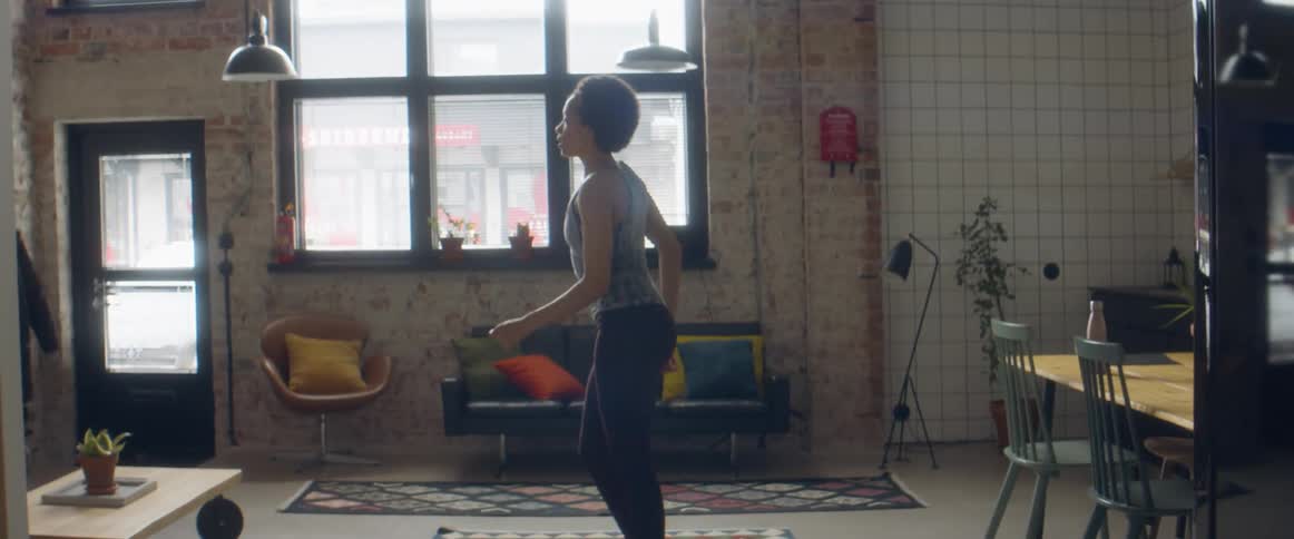 A woman bends over and stretches her arms before standing up and dancing on a rug in her living room