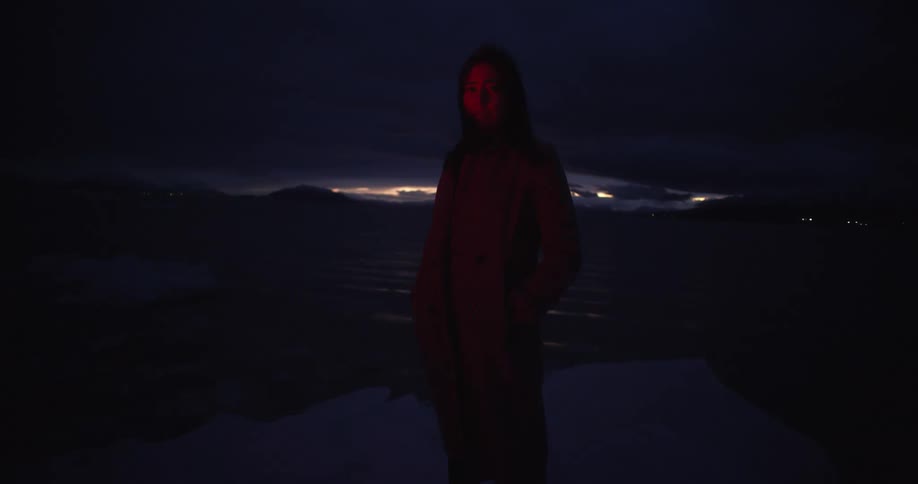 A woman standing by a lake with red flashing lights with glaciers with the sky and clouds in the background