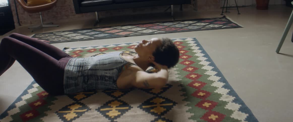 A woman does sit ups in a living room at home then stops to take a breather
