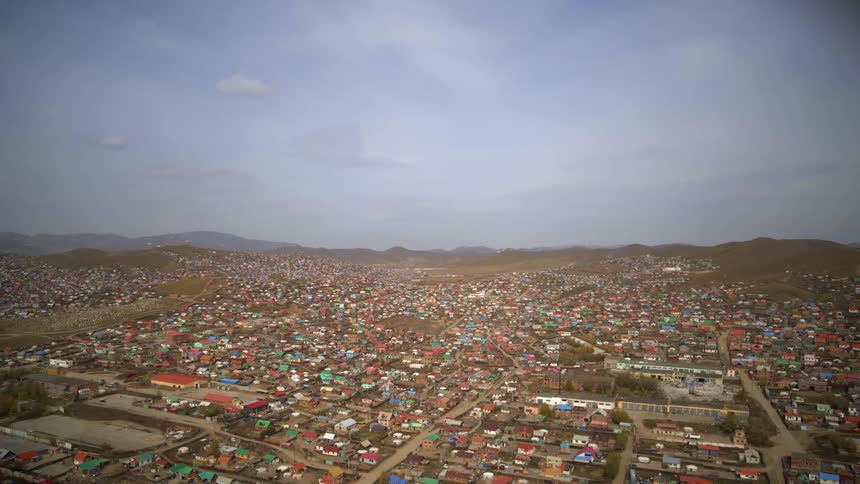 Town of colorful buildings stretches to low mountains on the horizon under a cloudy sky