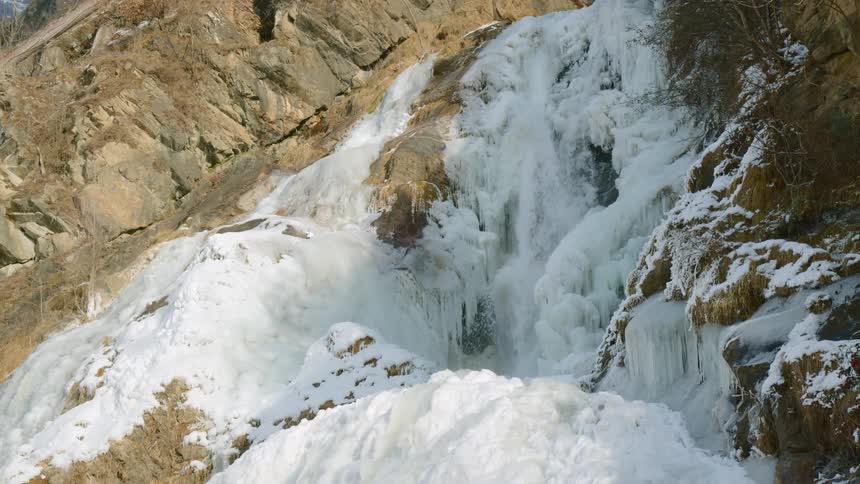 A river and a waterfall in the side of a cliff with ice and snow