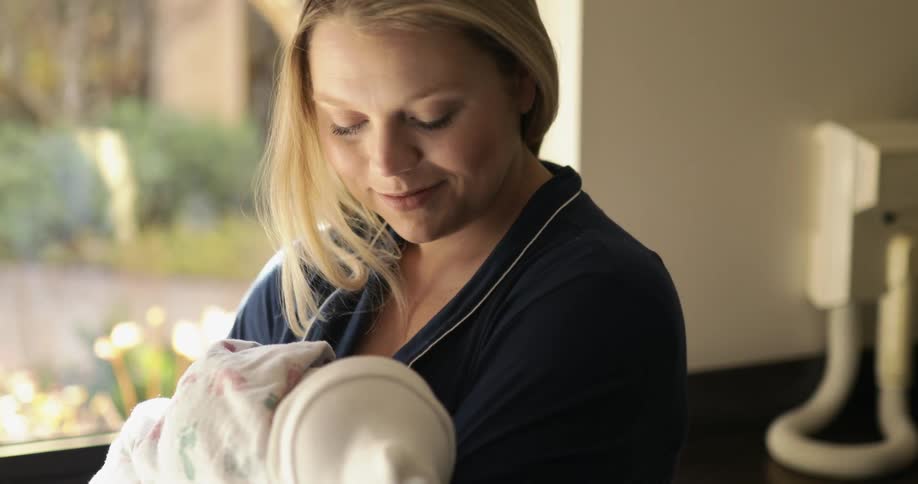 A woman smiles as she rocks her newborn baby in their hospital room