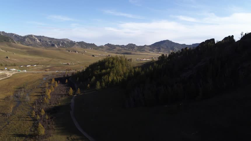 A valley between two mountain ridges containing a road and scattered buildings during the day