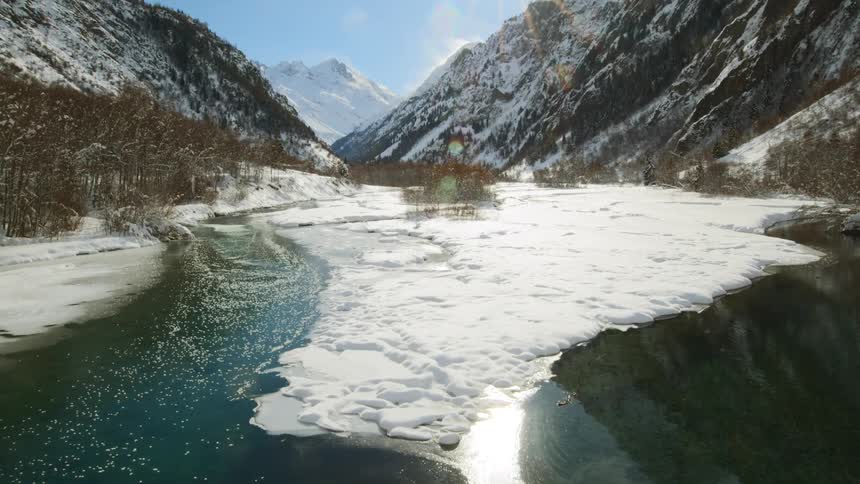 Bright sunlight reflects off a river that runs between snow covered mountains