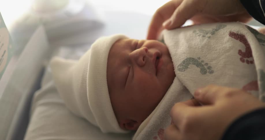 Person adjusts blanket wrapped around sleeping infant