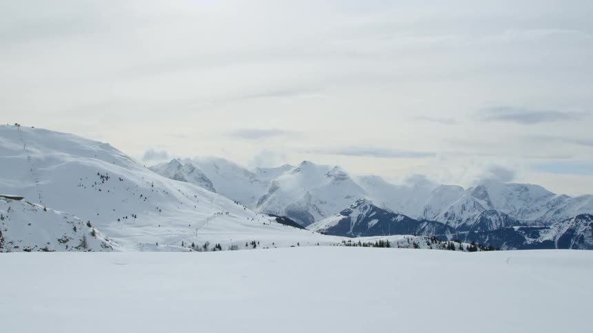 Trees peak through a thick blanket of snow covering a field and nearby mountain range