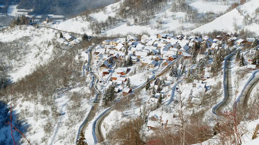 Car travels around road winding through snow covered town bordered by forests on snowy slope