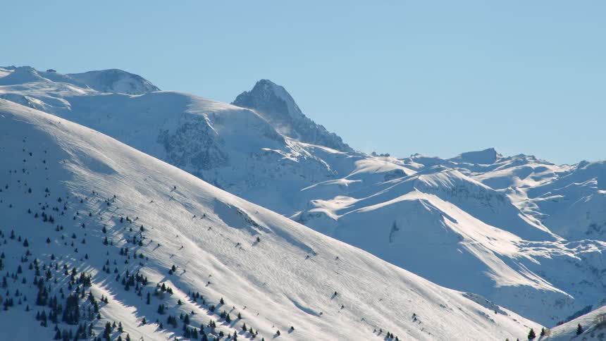Heavy snow blankets mountains slopes and forest under a clear blue sky