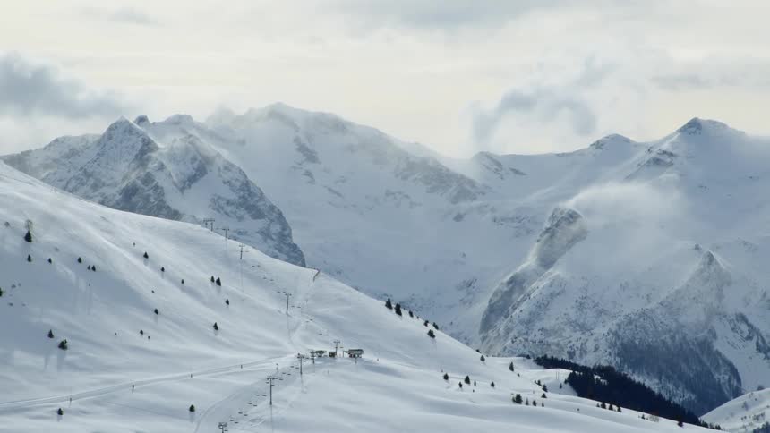 A mountain range covered in snow and ice with the sky and clouds in the background