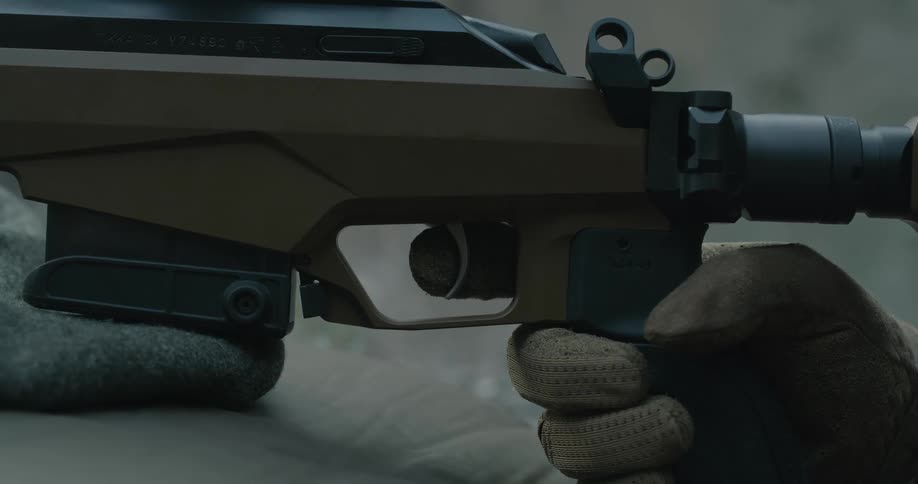 Person wearing gloves gently squeezes trigger of weapon set on flat surface