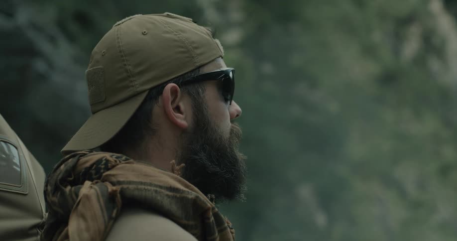 A man with a hat sunglasses and a backpack standing with a cliff in the background