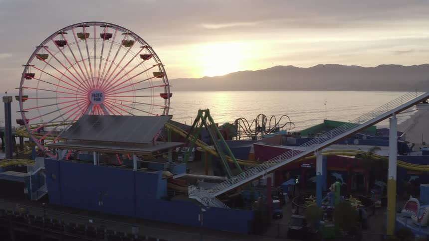 A long roller coaster and a tall ferris wheel loom above a boardwalk next to the ocean