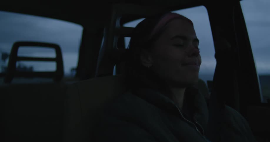 Woman wearing jacket smiles while driving car under overcast sky