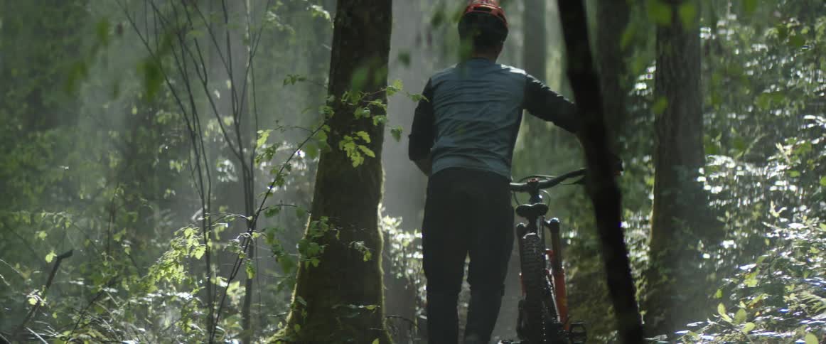 A cyclist pushes a bicycle through a forest during the day