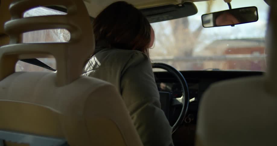 A woman driving a vehicle and turning the steering wheel with the sky and clouds in the background