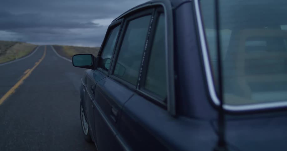 Car turns onto road bordered by fields under overcast sky