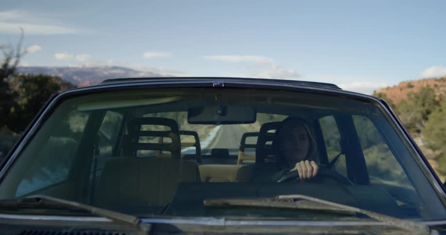 Woman wearing a hoodie driving a car on a rural road in the morning