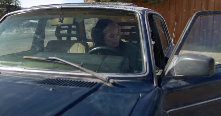 A woman with a jacket entering into a vehicle with a fence the sky and clouds in the background