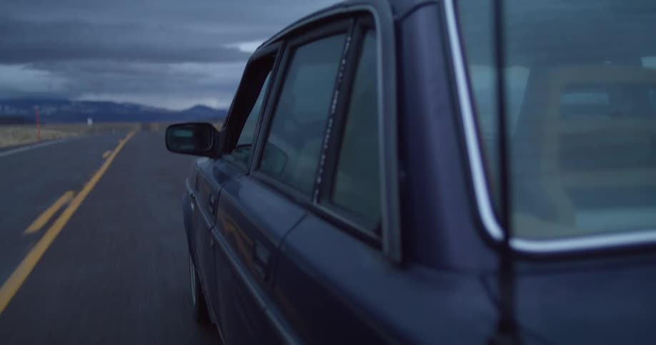 A person driving a vehicle and putting their hand out of the window with the sky and clouds in the background