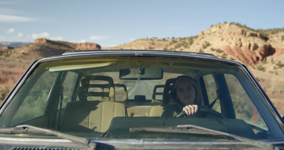 A woman driving a car on a remote road in the daytime