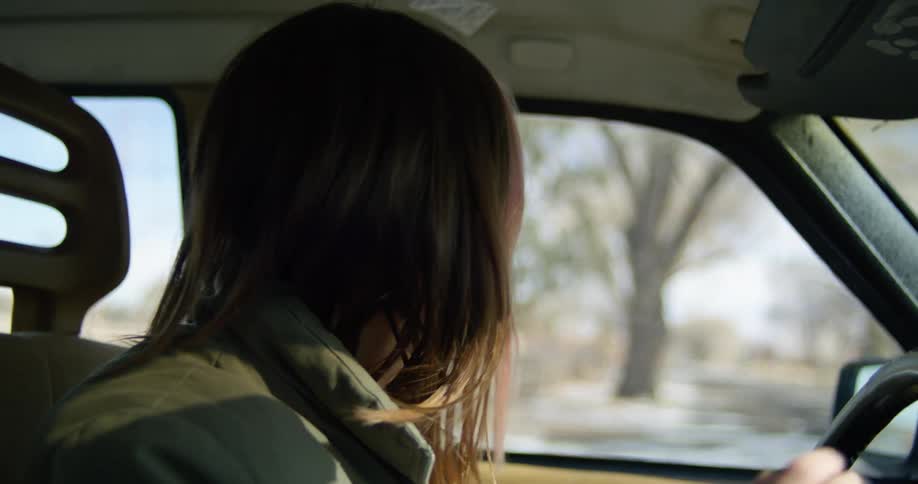 A woman driving a vehicle with trees the sky and clouds in the background