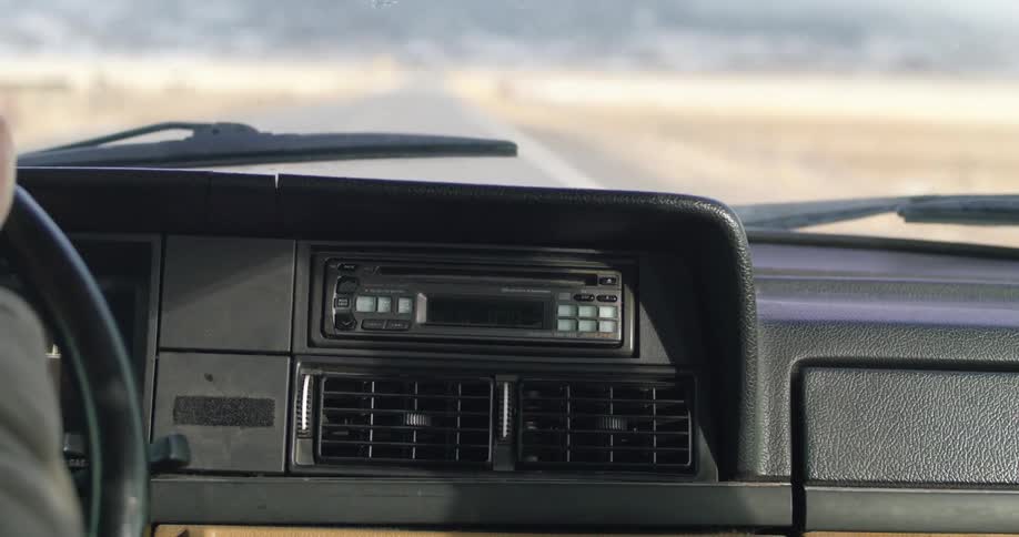 A person driving a vehicle and turning the steering wheel with the landscape and the road in the background