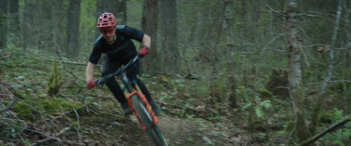 A man with a helmet riding a bike in a forest with trees through tight corners