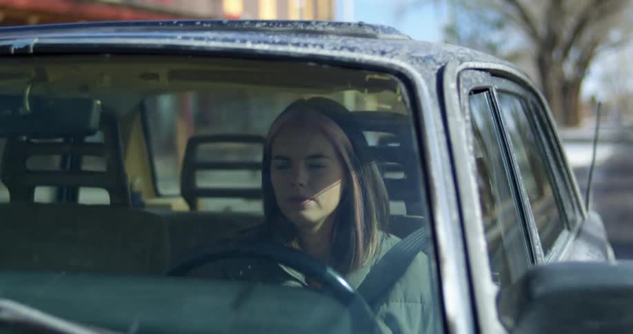 A woman sits behind the steering wheel of the automobile that she is driving along the street