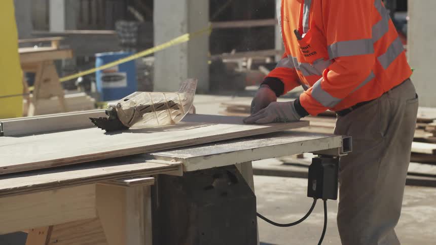 A construction worker cutting a piece of lumber with a saw on a construction site
