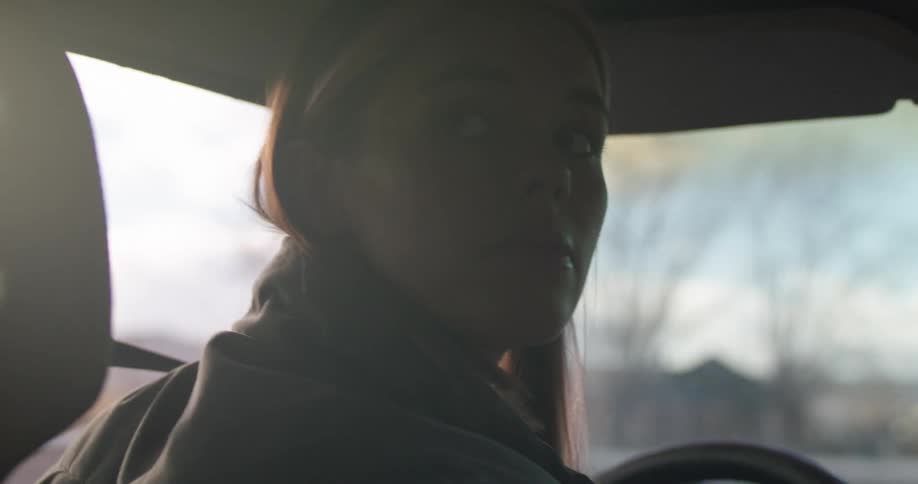A woman driving a vehicle and turning the steering wheel with the sky and clouds in the background