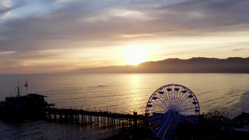 An aerial view of a pier with a ferris wheel on a beach at sunset