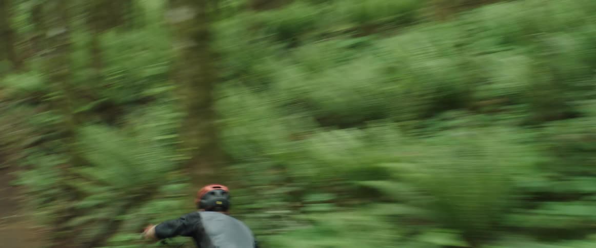A mountain bike athlete races full-speed down a lush forest trail