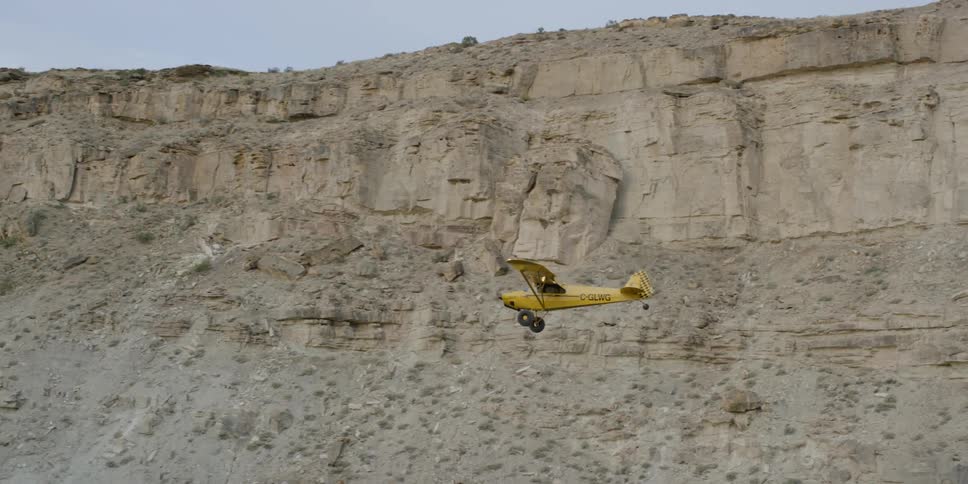 A yellow plane flying past a steep rock face