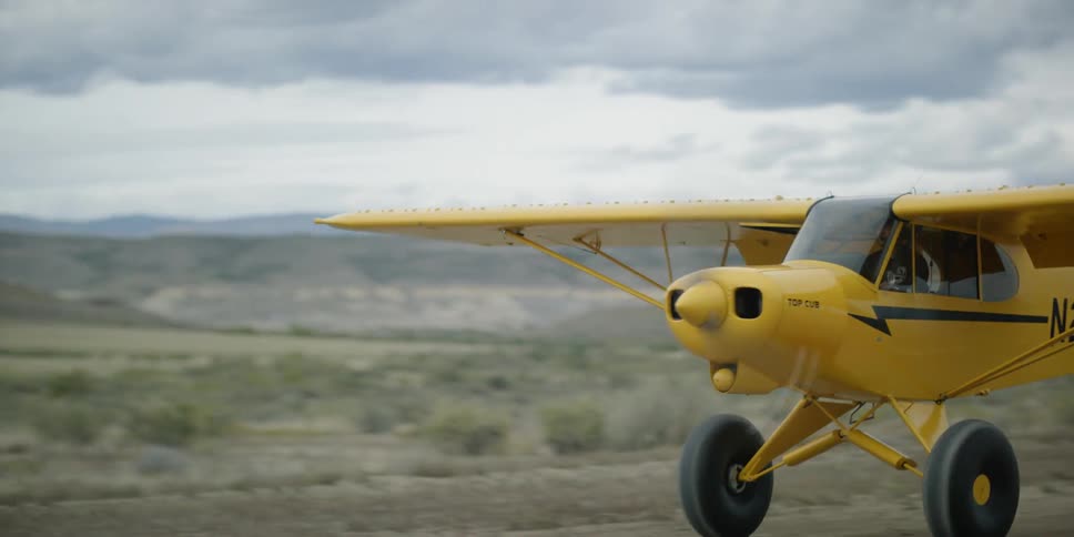 A small yellow single engine plane landing on a dirt runway in the desert