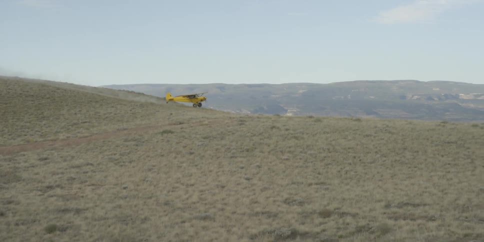A small yellow single engine plane landing on a dirt runway in the desert
