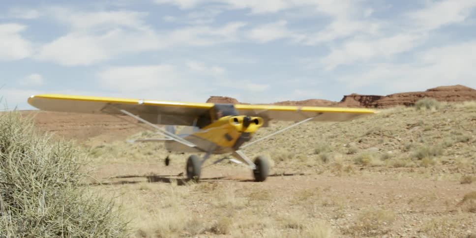 A yellow single engine plane takes off from a dirt runway in the desert in the daytime