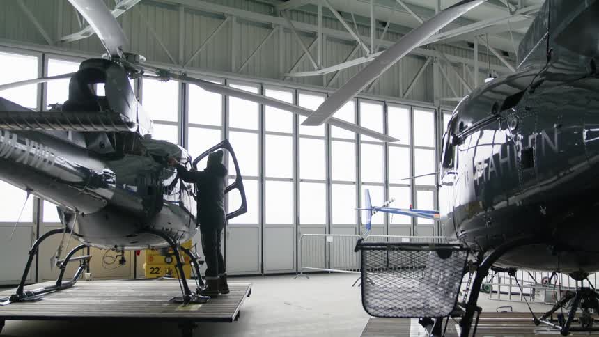 A person stands inside a large aircraft hanger beside a helicopter
