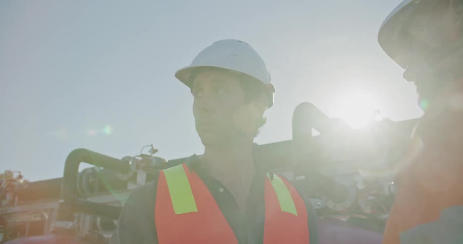 Construction workers wearing white hard hats talking in front of red container tanks