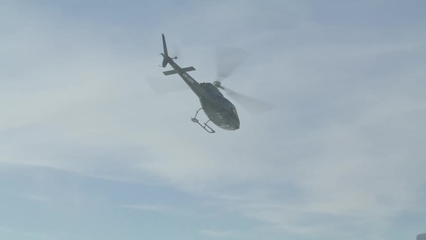 A helicopter flies over mountains in a cloudy sky