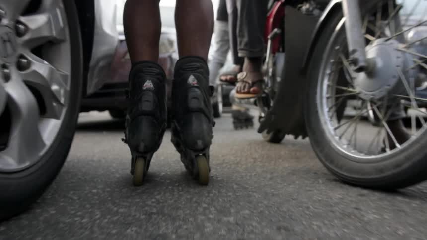 Two people roller blade between vehicles on a crowded roadway