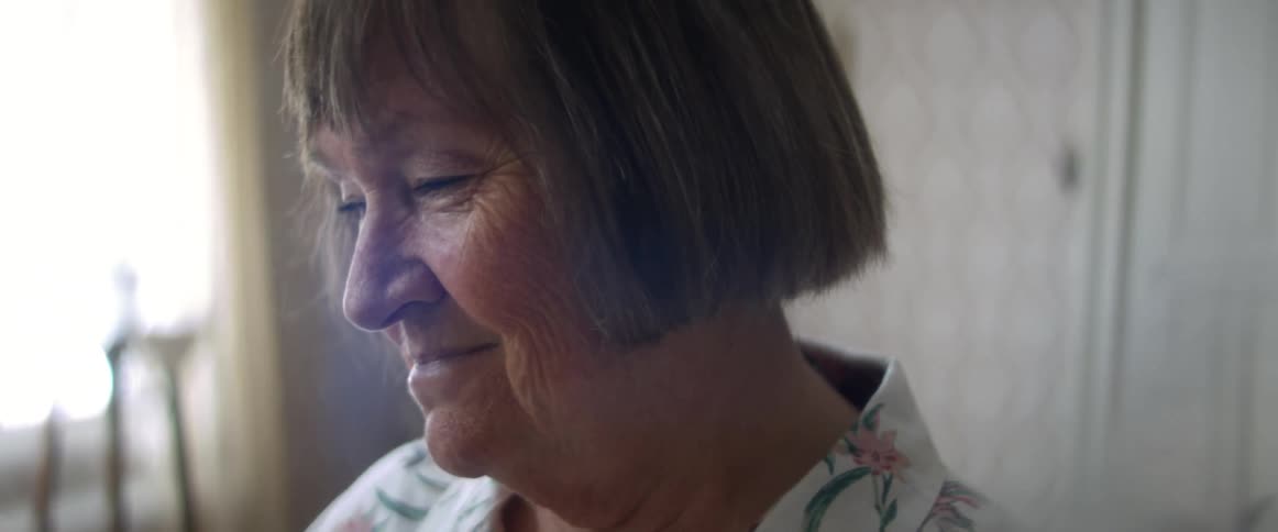 A woman in a room smiling with a wall and window in the background