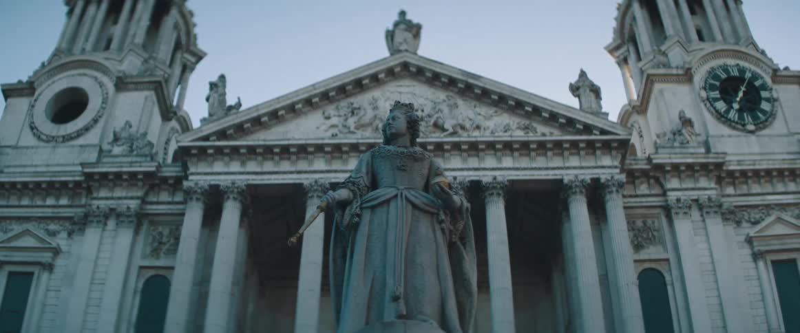 A statue with a building with pillars the sky and clouds in the background