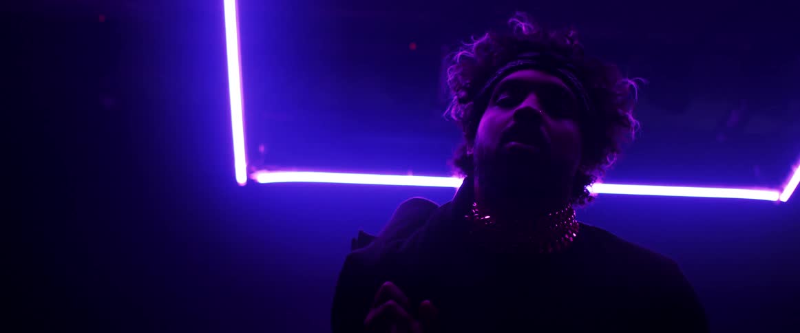 A man holds his jacket over his shoulder as he stands under neon lights