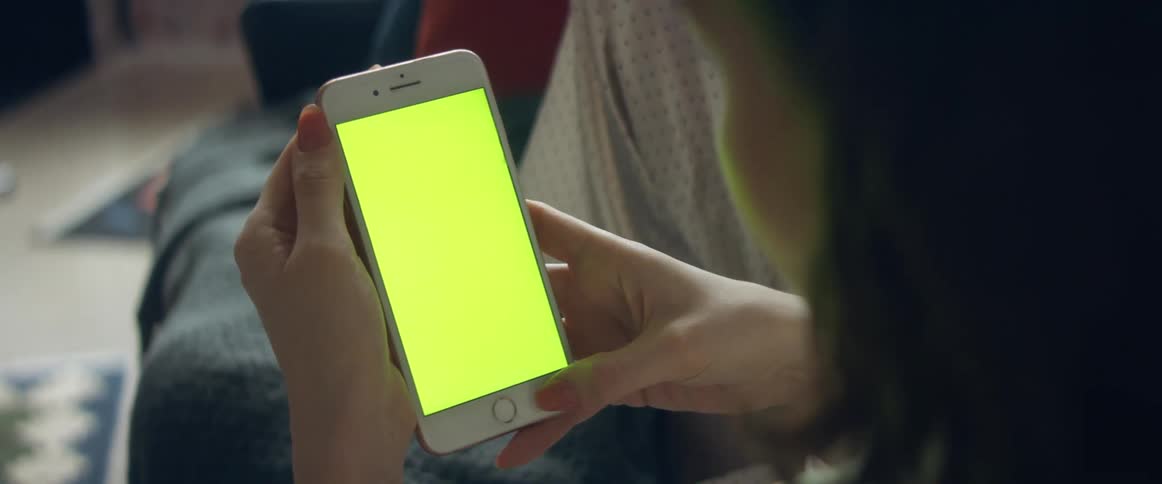 A woman reclines on a couch while looking at the screen of her smart phone