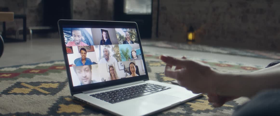 Woman sitting over a rug in the living room talking to a group of friends through a video call on a laptop
