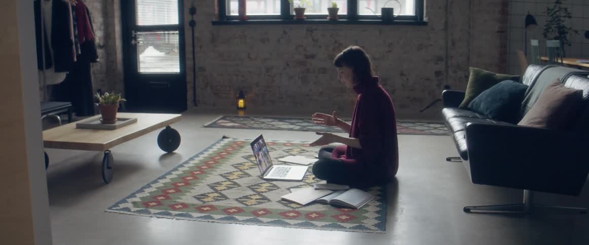 Woman sitting over a rug in the living room talking to a group of friends through a video call on a laptop