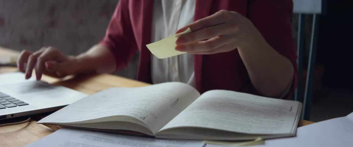 Woman working from home types the information from a post it into a laptop