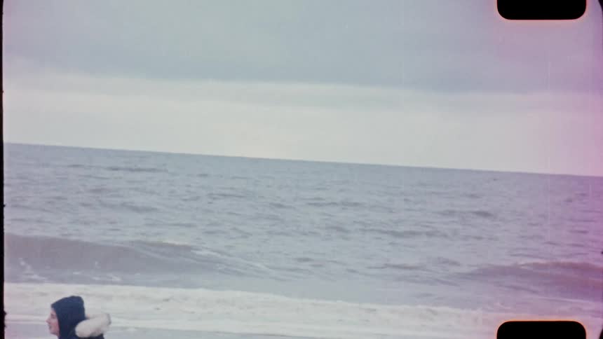 Ocean waves roll and a break upon a sandy beach as a person walks past on analog Film 16mm