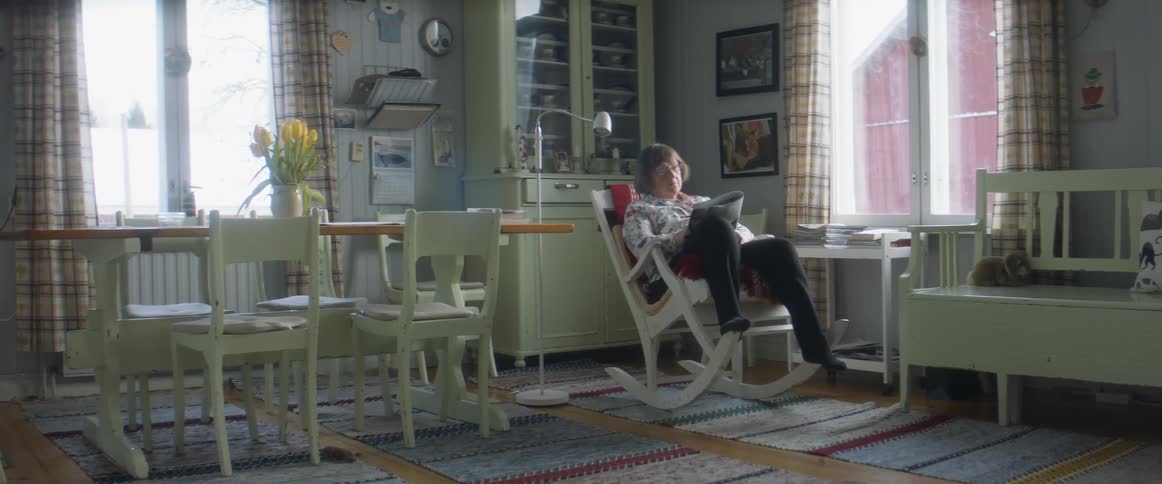 An older woman sits in a rocking chair reading a magazine