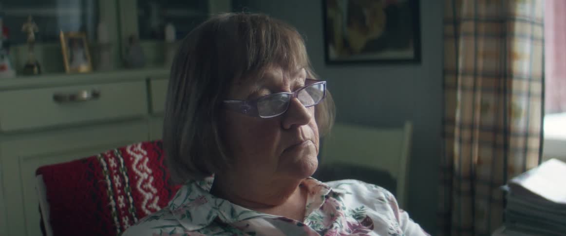 A woman sighs and takes off her glasses as she sits in her home